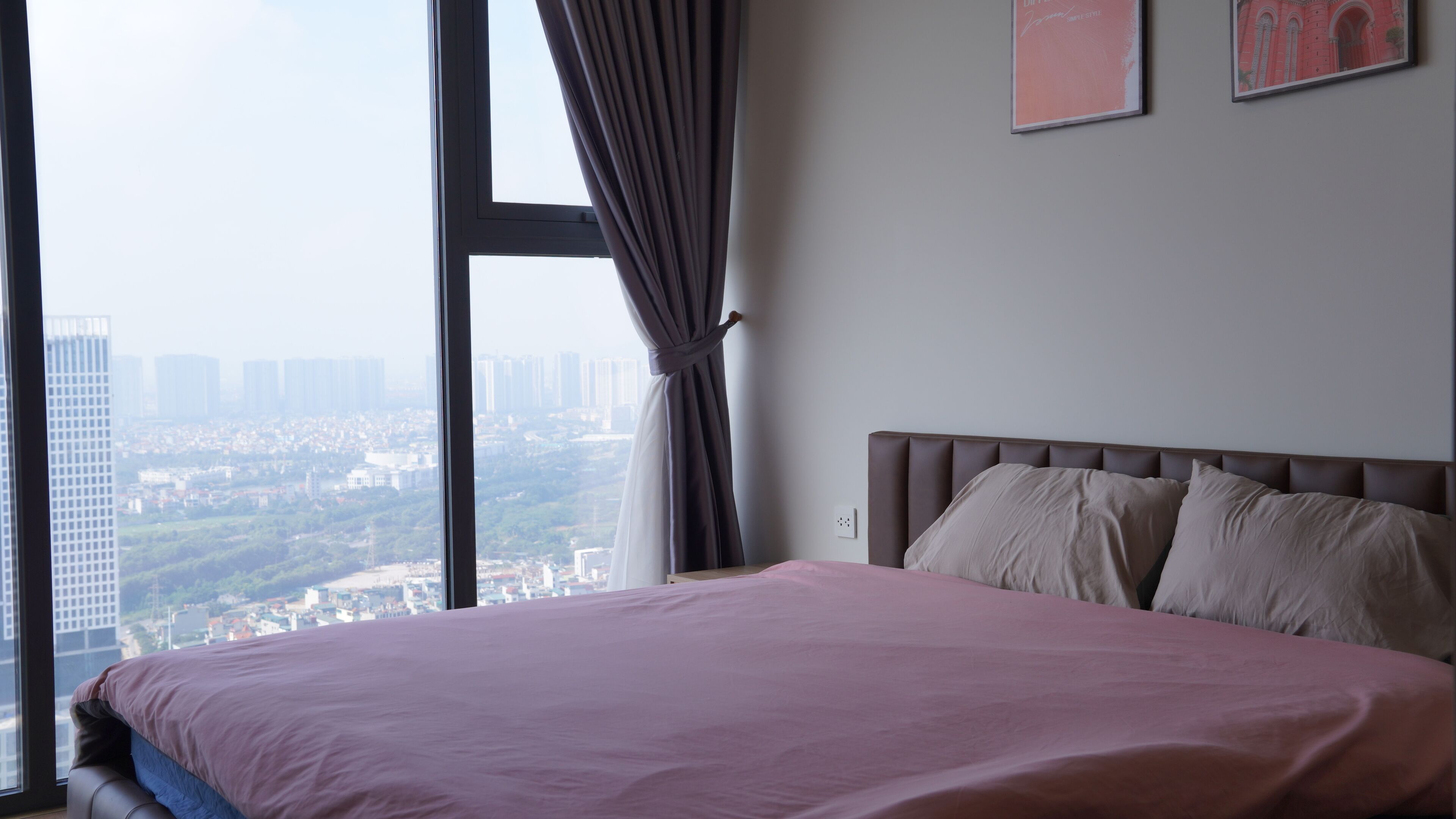 A bedroom with a bed, a window with curtains, and a city view.