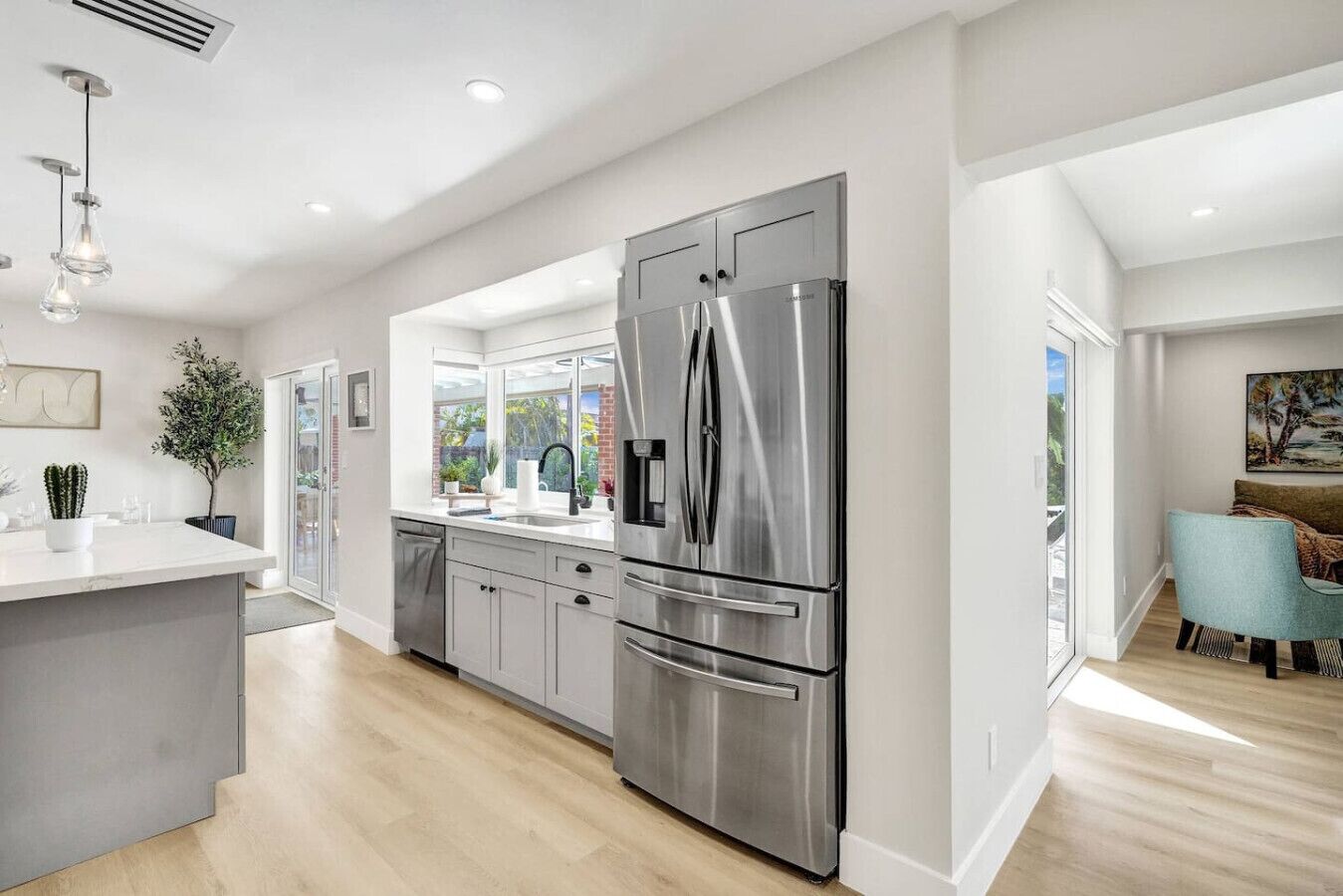 A modern kitchen with a large stainless steel refrigerator, a central island, and a dining area with a blue chair.