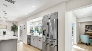 Eine moderne Küche mit einem großen, edlen Kühlschrank, einer zentralen Kochinsel und einem Essbereich mit einem blauen Stuhl.