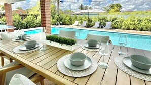 Ein Essbereich im Freien mit Blick auf einen Pool, Holztische und Lounge-Stühle.