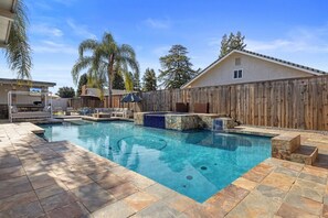 Relax by the pool surrounded by lush greenery and a wooden fence.