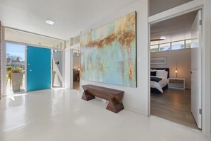 Contemporary hotel room with a large abstract painting, a wooden bench, and a neatly made bed.