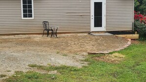 Une maison à deux étages avec une porte d’entrée, un petit porche avec une chaise et une allée gravillonnée.