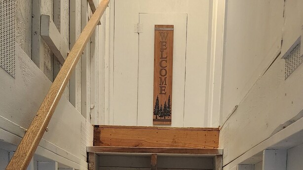 Un escalier avec des marches en bois et une rampe, menant à un palier où se trouve une enseigne en bois.