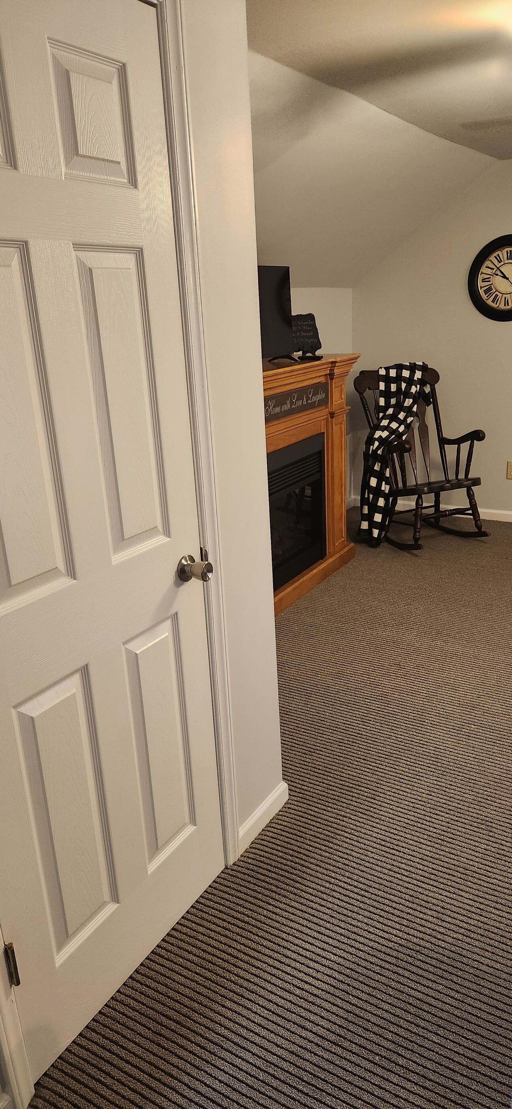 A room with a white door, a fireplace, a rocking chair, and a carpeted floor.