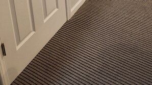 Une pièce avec une porte blanche, une cheminée, un fauteuil à bascule et un sol recouvert d’une moquette.