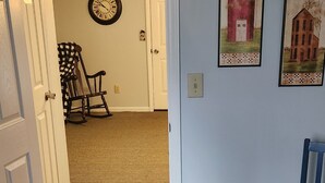 Une pièce dont le sol est recouvert d’une moquette, avec un lit recouvert d’une courtepointe, un fauteuil à bascule et deux tableaux encadrés accrochés au mur.