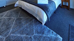 A bedroom with a bed, two bedside tables, a nightstand, a radiator, and two paintings on the wall. - Kingfisher Lodge Studio (Lake Tekapo)