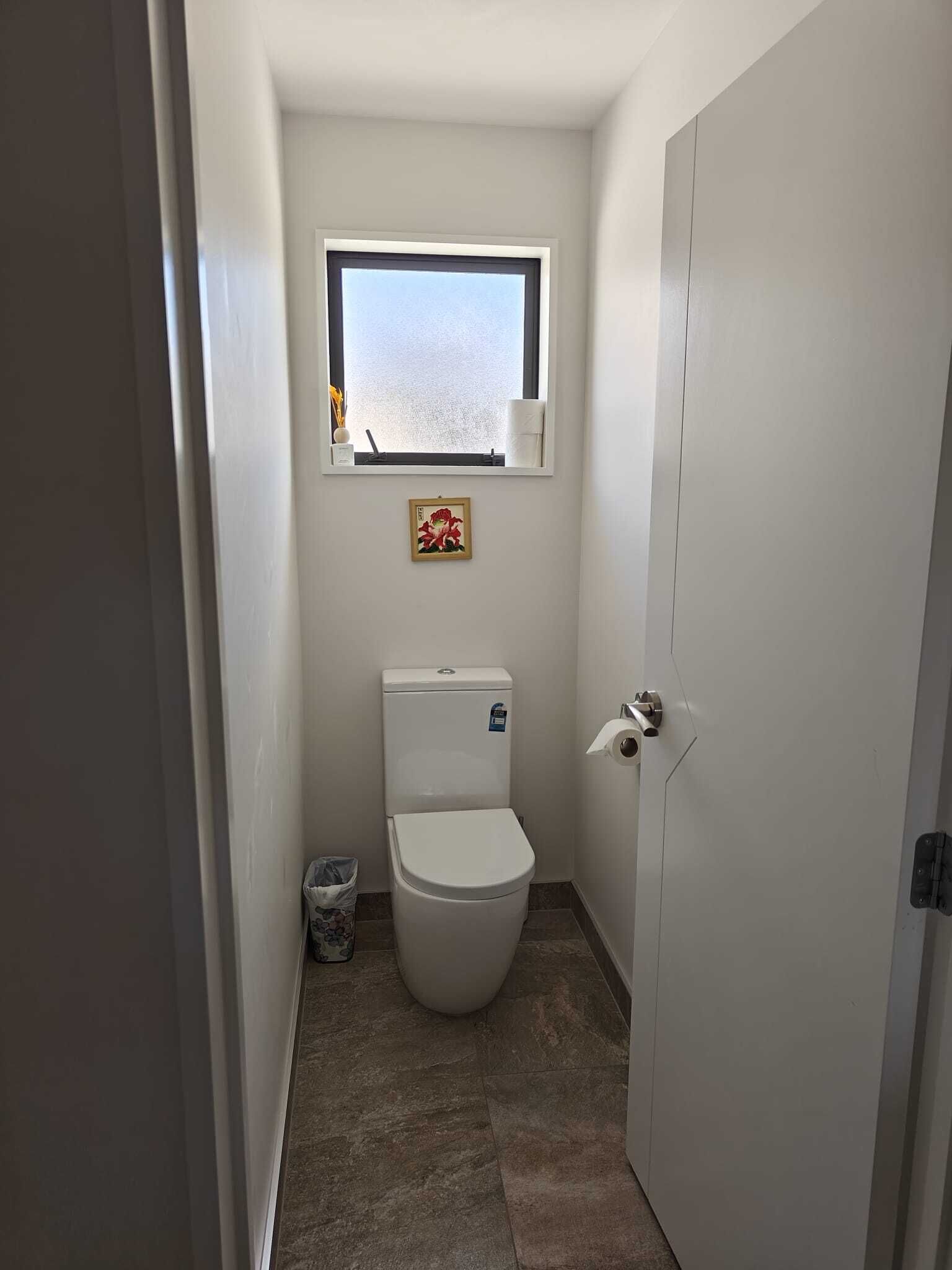 A small, narrow bathroom with a toilet, a window, and a door.