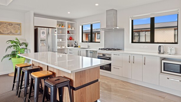 A modern kitchen with white cabinetry, a central island, bar stools, and a large window.
