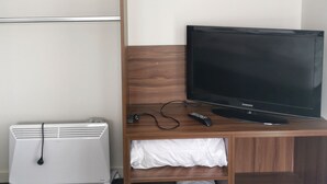 Et hotelværelse med et træ-tvbord, et Samsung-TV, en hvid aircondition og en billedramme på væggen med tre billeder.