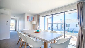 A modern dining area with a large table, white chairs, and a view of the outside.