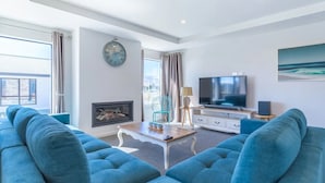 A modern living room with a large sofa set, a fireplace, a television, and a clock on the wall.