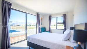 A modern hotel room with a large bed, a view of a lake, and a balcony.