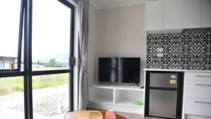 Ein modernes Wohnzimmer mit Fernseher, einer kleinen Kühlbox und einem Esstisch mit Schüssel und einem pinkfarbenen Gegenstand.