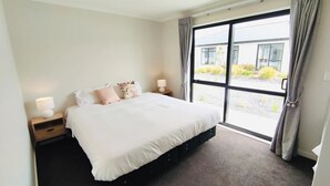 Ein modernes Schlafzimmer mit einem großen Bett, zwei Nachttischen mit Lampen und Blick auf ein Gebäude durch ein großes Fenster.