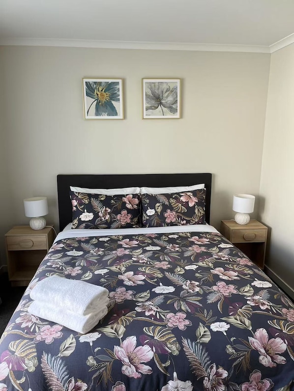 A neatly made bed with floral bedding, two framed artworks on the wall, and bedside lamps on wooden nightstands.