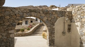 A stone archway leading to a building with a concrete pathway and a stone wall. - Seafront 9BDR Serenity in Mykonos (Mikonos)