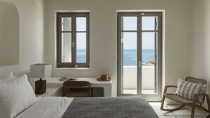 A bedroom with a bed, a desk, a rocking chair, and a view of the sea through a large window. - Seafront 9BDR Serenity in Mykonos (Mikonos)