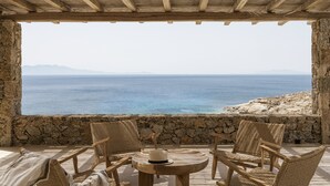 A stone-walled room with a wooden ceiling, a round table, and wicker chairs. - Seafront 9BDR Serenity in Mykonos (Mikonos)