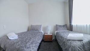 A twin room with two beds, each with a grey floral bedspread, a white pillow, and a white towel on the bed. There is a nightstand with a lamp between the beds. - Starry Heaven 2bdr2ba (Lake Tekapo)