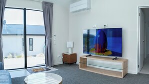 A modern living room with a flat-screen TV, a sofa, a glass coffee table, and a sliding glass door leading to an outdoor area. - Starry Heaven 2bdr2ba (Lake Tekapo)