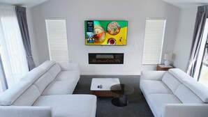 A modern living room with two white sofas, a coffee table, a flat-screen TV mounted on the wall, and a fireplace below. - Starry Heaven 3bdr3ba (Lake Tekapo)