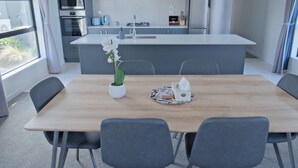 A modern kitchen with grey cabinets, a central island, and a dining area with a wooden table and grey chairs. - Starry Heaven 3bdr3ba (Lake Tekapo)
