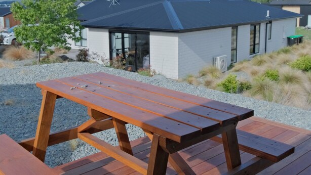 A wooden deck with a picnic table, a modern building with a dark roof, and a mountain range in the background. - Starry Heaven 3bdr3ba (Lake Tekapo)