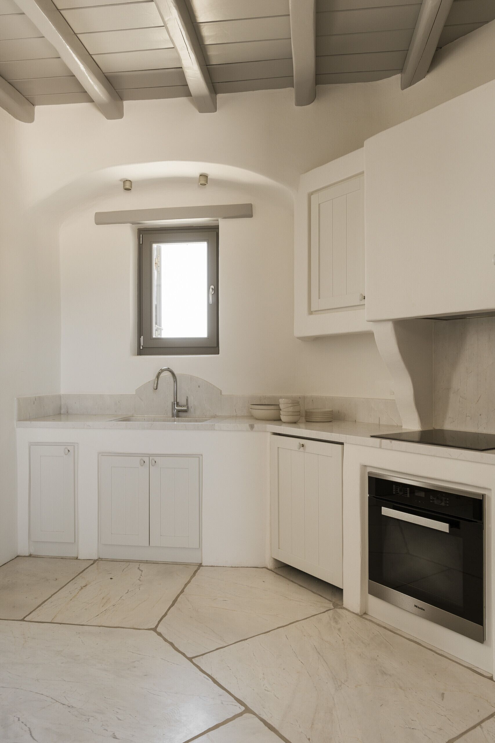 A modern kitchen with white cabinetry, a built-in oven, and a window above the sink.
