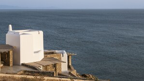 A white building with a stone base near the sea, overlooking the water. - Luxury 5BDR Retreat in Mykonos (Mikonos)