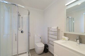 Ein modernes Badezimmer mit Duschkabine aus Glas, Toilette, Handtuchhalter und Waschbecken mit Spiegel.