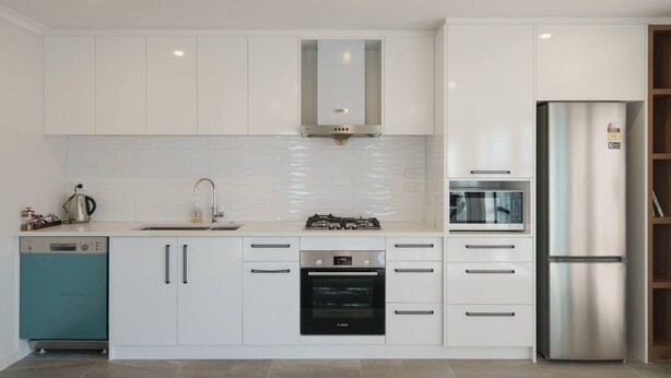 A modern kitchen with white cabinets, a stainless steel refrigerator, a dishwasher, and a built-in oven.