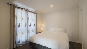A hotel room with a large bed, a bedside table with a lamp, and a window with curtains.