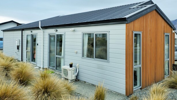 Un bâtiment moderne, de plain-pied, dont la façade combine un revêtement blanc et des éléments en bois, avec de grandes fenêtres et un petit appareil de climatisation installé au niveau du rez-de-chaussée.