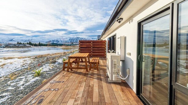 A wooden deck with a table and chairs, a glass door, and a view of mountains and a lake. - Mirror Lake 2 Bedroom A (Lake Tekapo)
