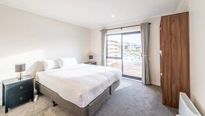 Une chambre avec un grand lit, une table de chevet, une commode, une porte en bois et une vue sur l’extérieur.