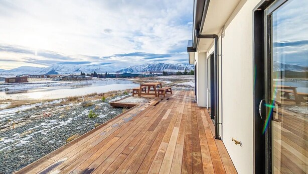 Une terrasse en bois avec une table et des chaises, d’où l’on peut admirer un paysage enneigé avec des montagnes à l’horizon.
