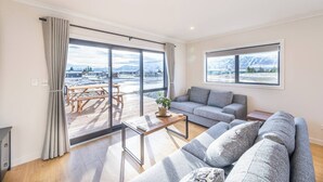 Un salon moderne avec un canapé gris, une table basse en bois et une vue sur un paysage enneigé, visible à travers de grandes fenêtres.