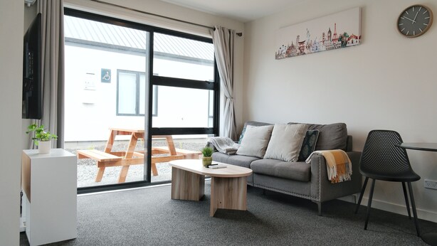 Ein modernes Wohnzimmer mit einem grauen Sofa, einem Holztisch, einem schwarzen Sessel und einem weißen Schrank.
