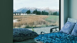 Un lit donnant sur un champ et des montagnes, vu à travers une fenêtre.