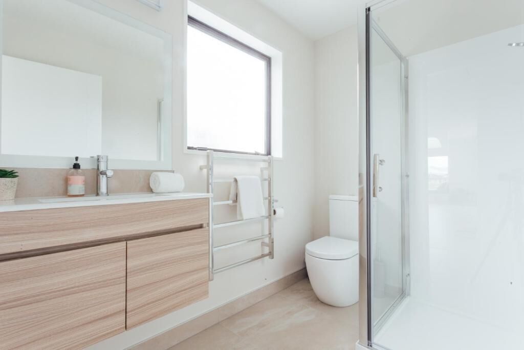 A modern bathroom with a wooden vanity, a large mirror, a toilet, and a glass shower enclosure.