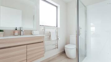 A modern bathroom with a wooden vanity, a large mirror, a toilet, and a glass shower enclosure.