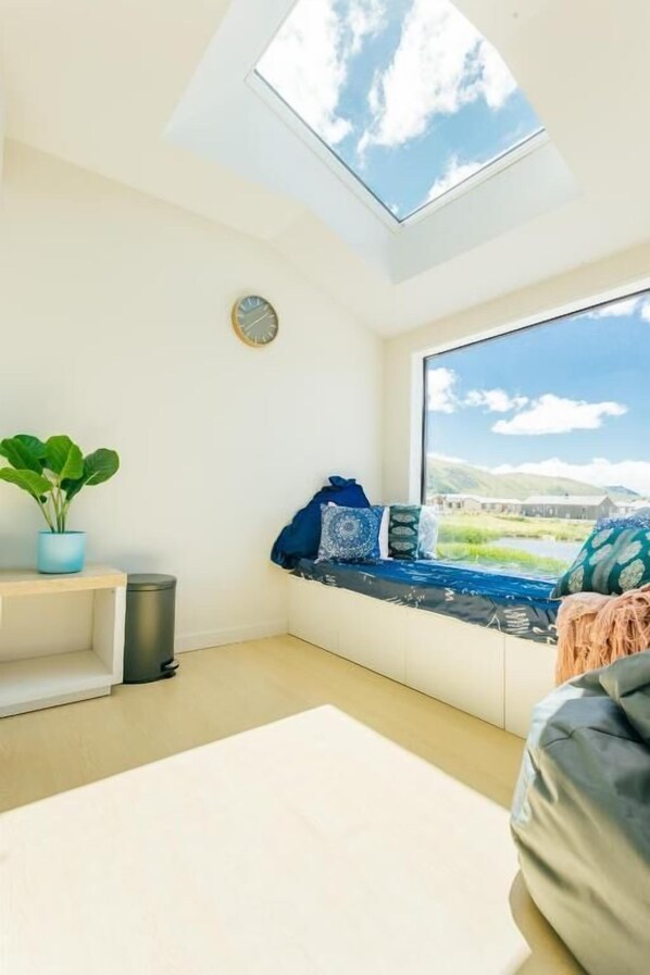A cozy room with a skylight, a large window with a view of a landscape, a small plant, and a bench with cushions.