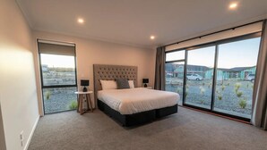Une chambre moderne avec un grand lit, une petite table de chevet et une vue sur un parking, visible à travers une porte coulissante.