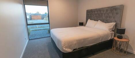Un dormitorio moderno con una cama grande, una mesita de noche y vistas a un espacio exterior por una puerta corrediza.