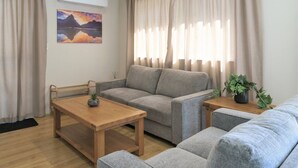 A living room with a grey sofa, a wooden coffee table, and a small side table with a plant. - Jeros 2bdr Apartment (Lake Tekapo)