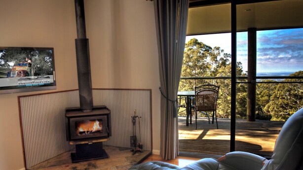 A cozy living room with a fireplace, comfortable seating, and a balcony with a scenic view. - Deluxe King Studio - Cedar (Ocean View)