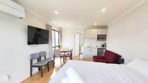Une chambre d’hôtel comprenant un lit, une télévision, un bureau, une chaise, un canapé rouge et une kitchenette.