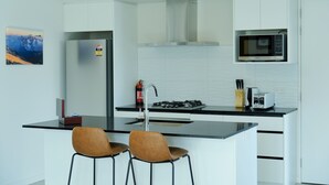 Una cocina moderna con armarios blancos, un refrigerador de acero inoxidable, un microondas, una estufa a gas y dos taburetes de bar.